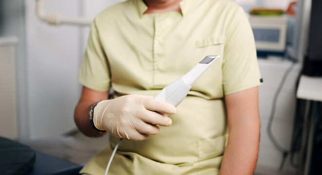 Dental professional wearing a medical glove holds a digital intraoral scanner in a modern dental clinic, illustrating digital dentistry, oral scanning, dental diagnostics and technology.