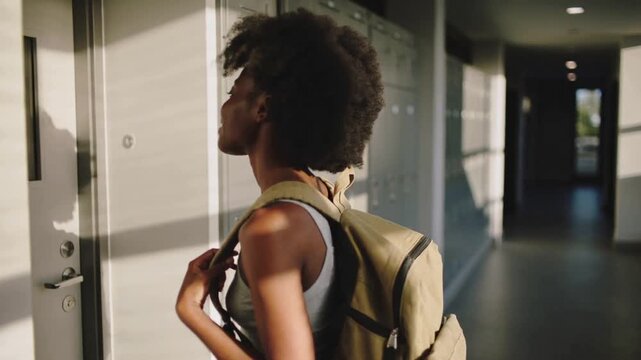 Spotting locker Black student in tank top holding backpack straps approaching school locker to open