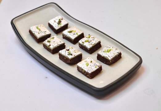 Chocolate barfi or barfee decorated with silver coating and pistachio on a white plate