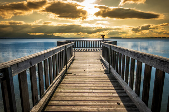 wooden pier with mountains in the distance, reflecting on calm water in the early morning light