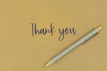 Gold pen isolated on a gold background. Greeting card with the words 'Thank you'. Thank you card with copy space. © nipa