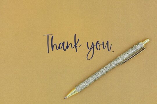 Gold pen isolated on a gold background. Greeting card with the words 'Thank you'. Thank you card with copy space.