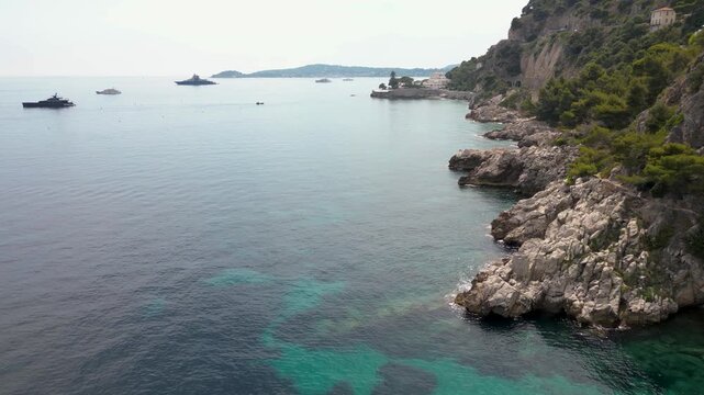 Aerial drone view of Plage des Pissarelles nudist naturist beach hidden cove with turquoise clear sea, dramatic rocky cliffs and yacht in Cap d'Ail, French Riviera, France 