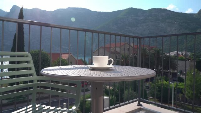 Woman&rsquo;s hand placing a white cup on a table on a sunny summer balcony, cozy outdoor lifestyle and relaxing morning coffee concept