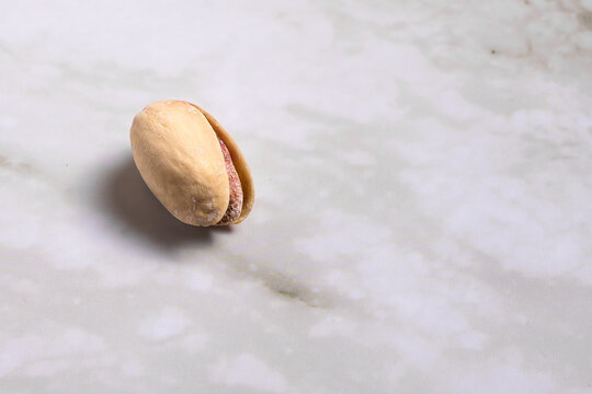 Salted pistachios with open shell isolated on light marble surface, top view composition with negative space, healthy snack background