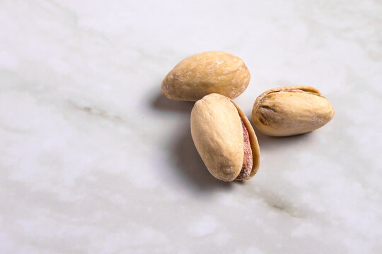 Salted pistachios with open shell isolated on light marble surface, top view composition with negative space, healthy snack background