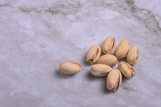 Salted pistachios with open shell isolated on light marble surface, top view composition with negative space, healthy snack background