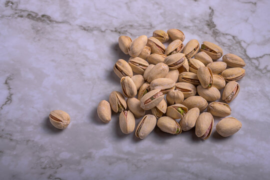 Salted pistachios with open shell isolated on light marble surface, top view composition with negative space, healthy snack background