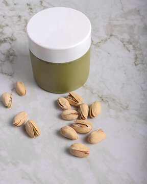 jar of creamy pistachio butter with whole nuts on marble surface, gourmet food concept, copy space