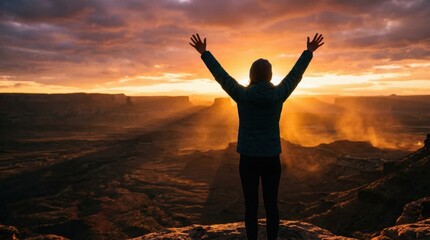 Fototapeta premium Woman arms raised in triumph on mountain peak at sunset with sun rays over canyon landscape