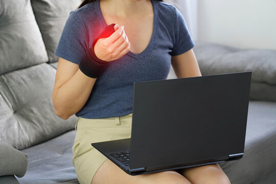 Young Woman Wearing Hand Brace for Tendonitis while Working on Laptop at Home. Red Highlight on Inflamed Area.