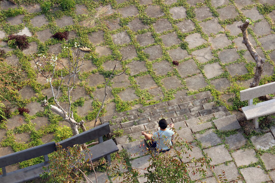 High angle view of a man meditating in lotus position on a stone paved terrace with green grass in cracks.