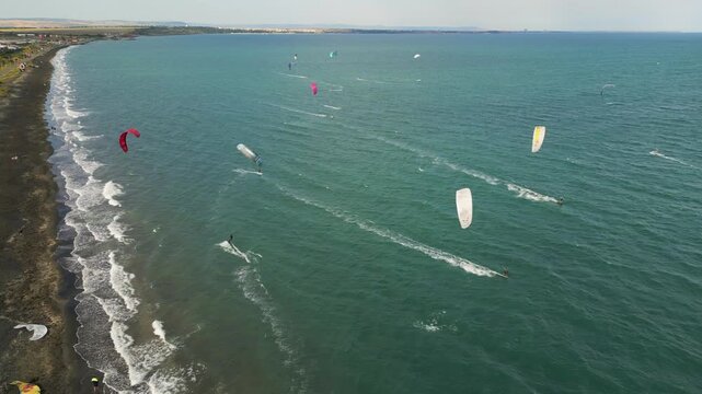 Kitesurfers Riding Waves along Dark Sand Beach Coastline on Windy Day