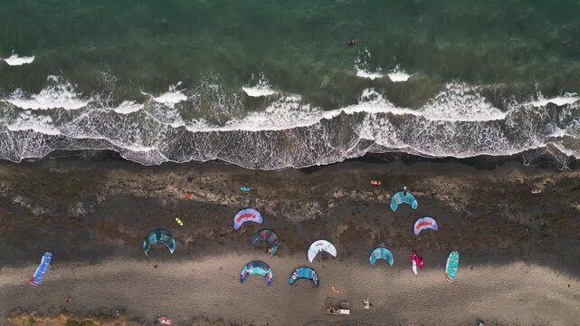 Aerial Top-Down View of Kitesurfing Kites on Dark Sand Beach and Waves