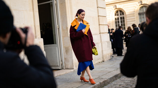 Young woman in colorful coat walking past photographers at fashion show  