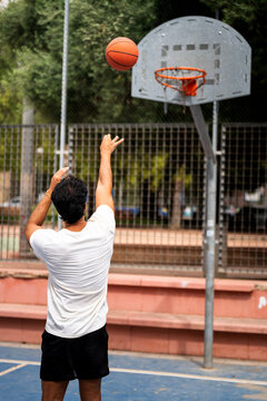 Man shooting basketball on urban court, playing streetball, enjoying outdoor sport