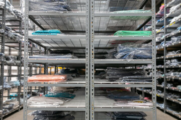 Well-organised industrial stockroom or e-commerce warehouse featuring multi-tier metal shelving with slotted uprights and deck shelves, neatly arranged with plastic-wrapped apparel inventory © Val
