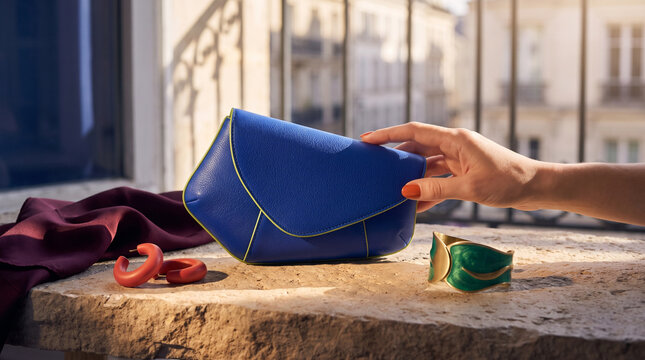 Woman reaching for a blue leather handbag on a stone table  