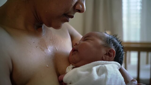 Cradling mother holding newborn on bare upper chest in nursery, with muslin swaddle for bonding
