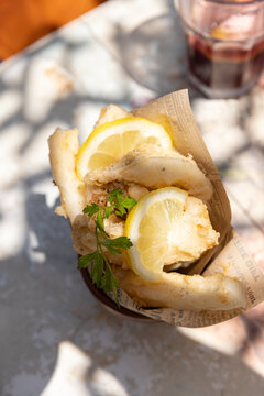 fried calamari garnished with lemon and cilantro on an outdoor restaurant patio with dappled light