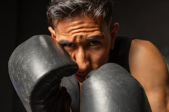 Close up Hispanic boxer protecting face with gloves against black background
