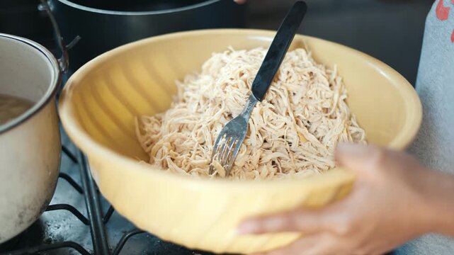 Close up of female hands shredding cooked chicken with a fork in a yellow bowl tinga