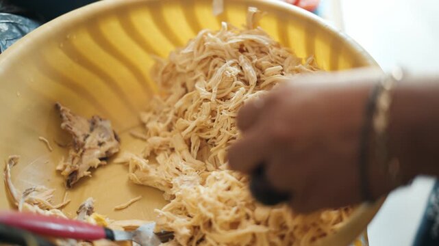 Close up of a woman's hands shredding boiled chicken breast in a yellow bowl for a recipe tinga