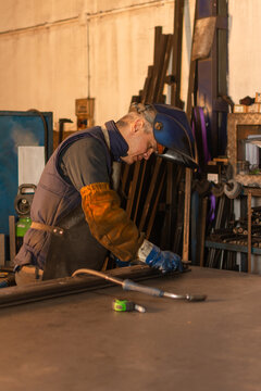 Industrial welder preparing metal piece with welding torch on workbench