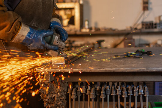 Side view of gloved hands grinding metal with electric grinder and sparks