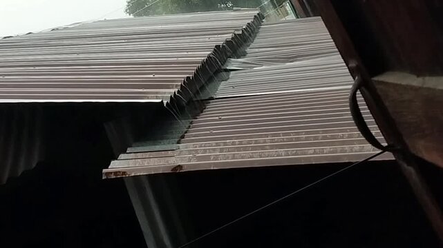 Heavy rain falling on an old zinc roof of a local community house, rustic tropical rainy season.