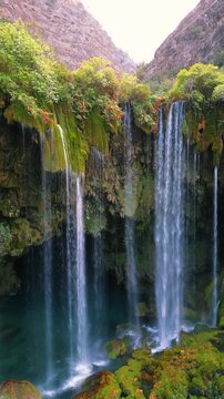 Scenic view of Yerkopru Waterfall cascading down a rocky cliff surrounded by lush green vegetation in Mersin, Turkiye. Natural landscape and flowing water in a Mediterranean mountain environment.