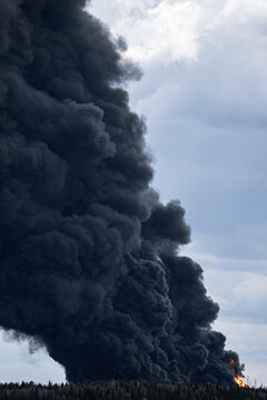 Massive plumes of dense black smoke rise from a large structure fire, indicating a major industrial incident involving the combustion of petroleum products and contributing to severe air pollution