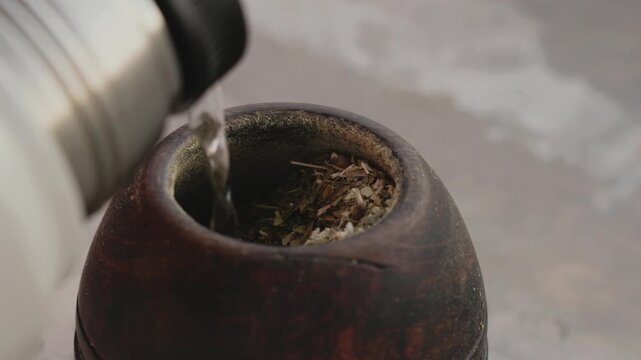 Close up of hot water being poured from a thermos into a calabash gourd with yerba mate tea