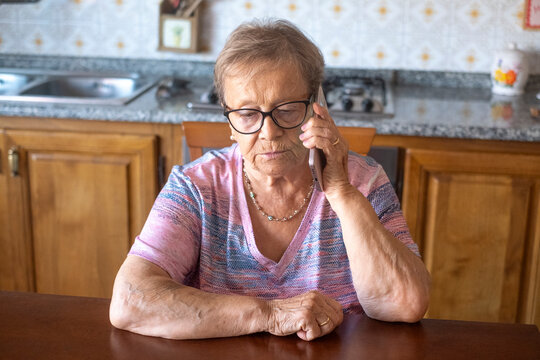 Elderly woman sitting at kitchen table talking on phone, a thoughtful senior in her home making a phone call
