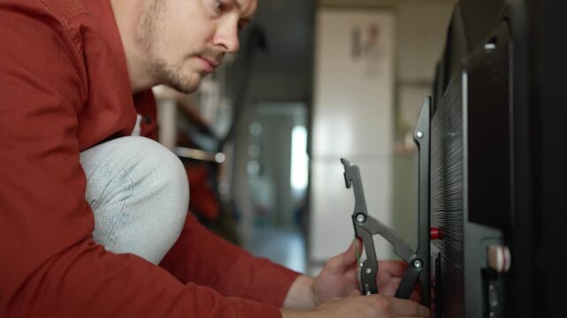 Focused man carefully installing a wall mount bracket on the back of his new television, concentrating on the assembly process for a home improvement and renovation project