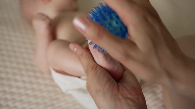 Close up of a mother's hands massaging her baby's foot with a spiky blue ball, focusing on newborn care, infant physical therapy, and early motor skill stimulation