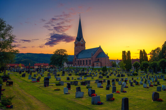 Colorful sunset silhouettes Lillehammer Church, a red brick steepled parish church, above a quiet cemetery in Lillehammer, Norway. It is also known as Lillehammer kirke.