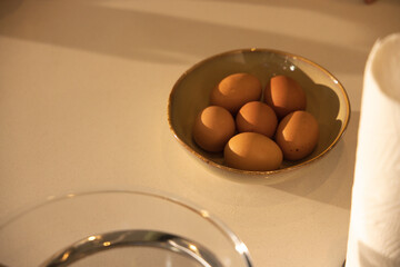 Ceramic bowl is sitting on countertop holding six brown eggs with blurred glass bowl, towel roll © WavebreakMediaMicro