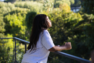 Woman leaning on balcony railing, holding cup with bracelet, gazing over sunlit hillside © WavebreakMediaMicro