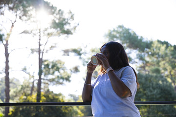 Adult African woman leaning on metal railing drinking from ceramic mug, wearing watch, copy space © WavebreakMediaMicro