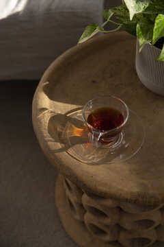 Clear glass teacup is resting on carved wooden side table near bed, sunlight casting amber glow