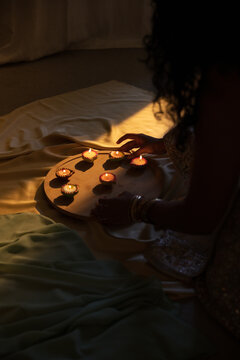 Round wooden tray is holding seven lit oil lamps on draped satin fabric, casting warm shadows