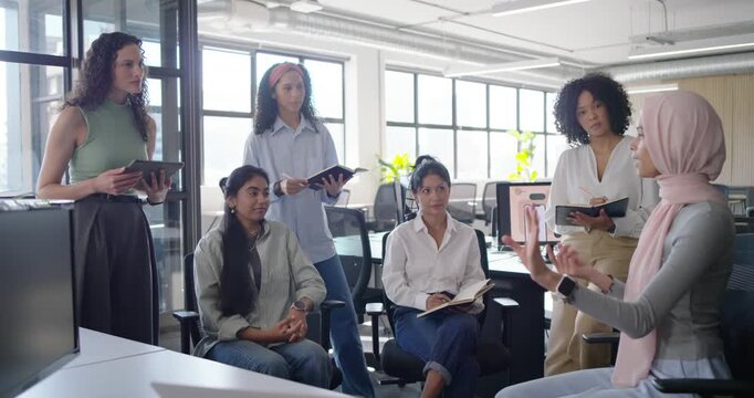 Diverse female coworkers taking notes after hijab speaker starting talk and gesturing, copy space