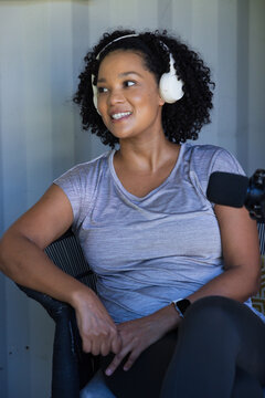 Woman sitting in woven chair in home studio wearing headphones and speaking into microphone