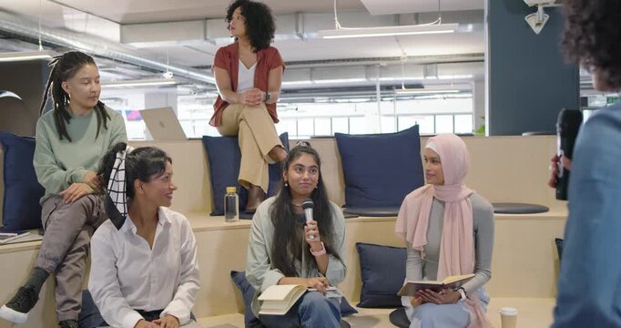 Diverse team passing microphone and speaking to discuss from notebook at office after host gesture