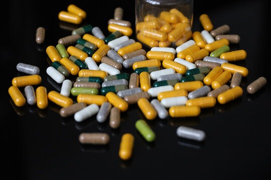 Pills in capsules scattered on a black glass table. Background for herbal medicine, antibiotics, vitamins, dietary supplements