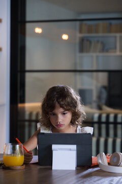 African American child sitting at table at home using tablet in black case holding pencil, notebook