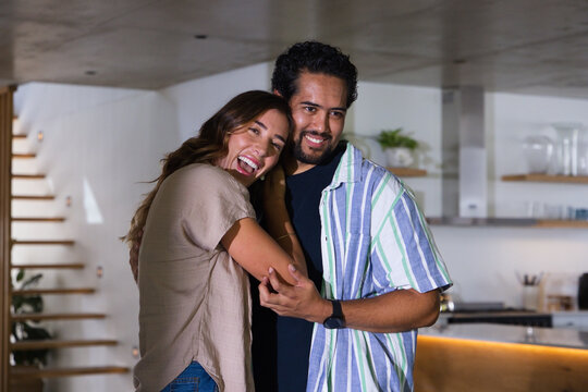 Couple woman and African American man laughing and hugging in modern kitchen by floating staircase