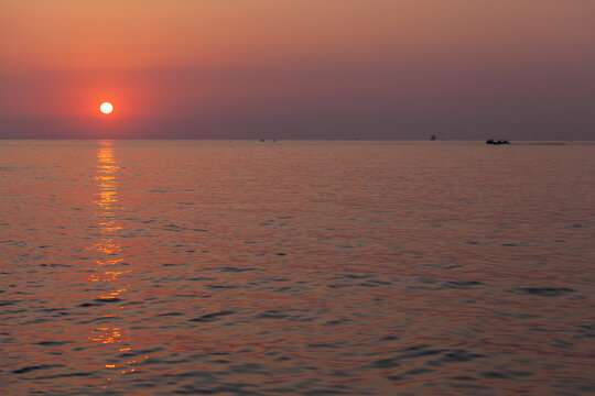 Sunset over a calm sea casts a golden reflection across rippling water while small boats silhouette on the distant horizon, evoking a peaceful, warm-toned seascape for travel and relaxation. Malta