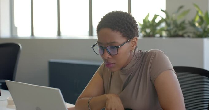 African American woman noticing laptop, leaning and tapping trackpad, editing document at desk